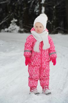 a little girl in a pink suit walks outside in winter.