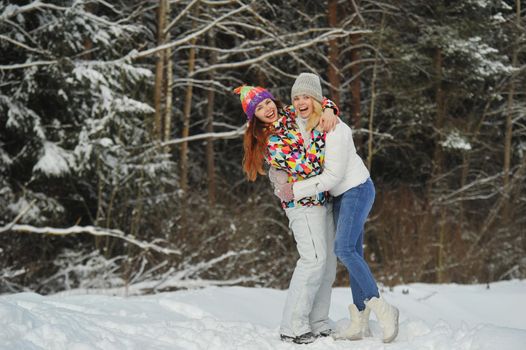 Two girls in the winter forest emotionally hug and smile.Happy women hug and Express joy.