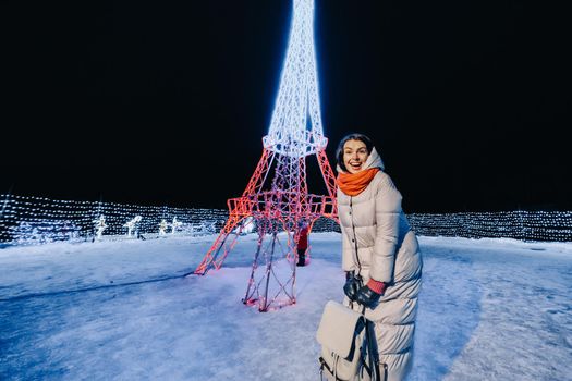 a girl in a gray jacket in winter with evening lights burning on Christmas street.