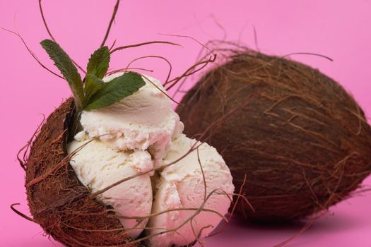Vanilla ice cream balls in an empty coconut decorated with mint leaves on a pink background.