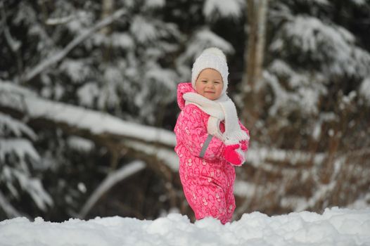 a little girl in a pink suit walks outside in winter.