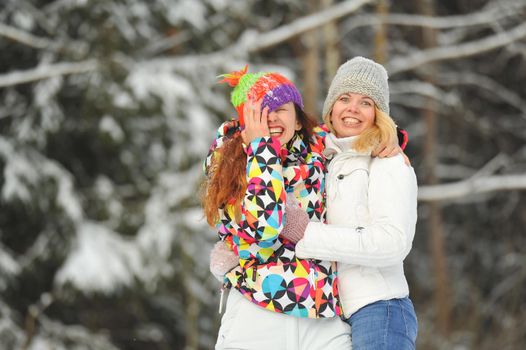 Two girls in the winter forest emotionally hug and smile.Happy women hug and Express joy.