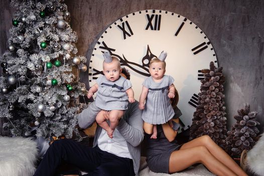 A happy big family with twin children in the New Year's interior of the house against the background of a large clock.