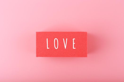 Word love written on red rectangle against pink background with copy space. Minimal trendy concept of Valentine's day, love emotions, anniversary or dating