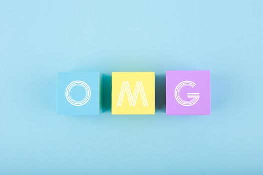 OMG written on multicolored cubes in a row in the middle of bright blue background. Bright, minimal, modern concept of emotions expression and being surprised or excited