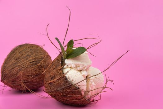 Vanilla ice cream balls in an empty coconut decorated with mint leaves on a pink background.