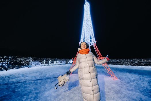 a girl in a gray jacket in winter with evening lights burning on Christmas street.