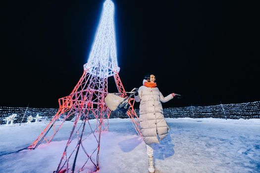 a girl in a gray jacket in winter with evening lights burning on Christmas street.