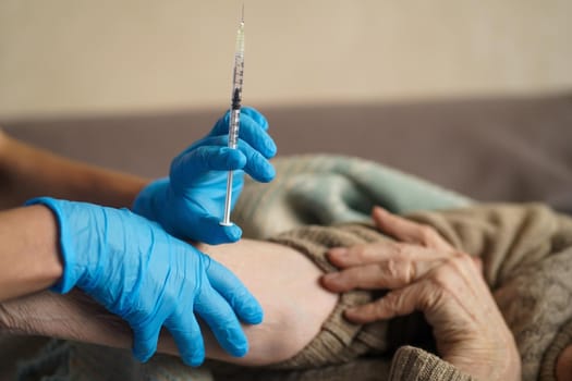 The nurse makes an injection with the vaccine to the patient at home. A young doctor in a blue suit holds the hand of an elderly woman and makes injection with a syringe. Medicine and healthcare.