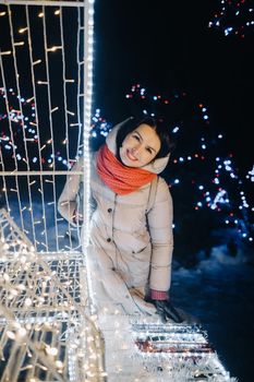 a girl in a gray jacket in winter with evening lights burning on Christmas street.