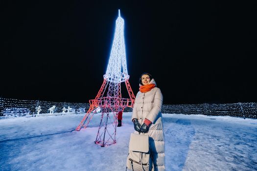 a girl in a gray jacket in winter with evening lights burning on Christmas street.