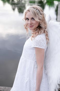 beautiful angel in white dress. Amazing blond woman with long curly hair and white wings