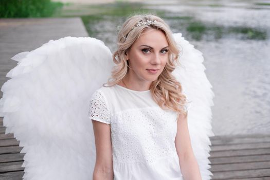 beautiful angel in white dress. Amazing blond woman with long curly hair and white wings