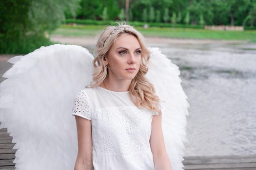 charming blonde with white angel wings standing by the water. beautiful woman in angel costume. goddess.