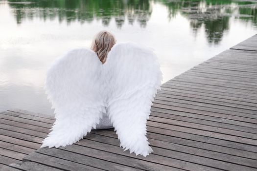 charming blonde with white angel wings standing by the water. beautiful woman in angel costume. goddess.