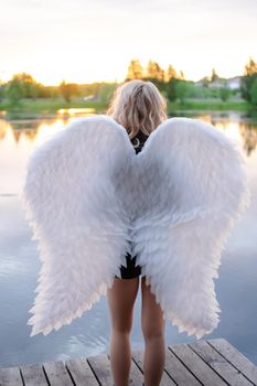 woman with white angel wings. wearing black leather clothes. fallen dark angel. demon. beast. girl in angel costume on halloween.