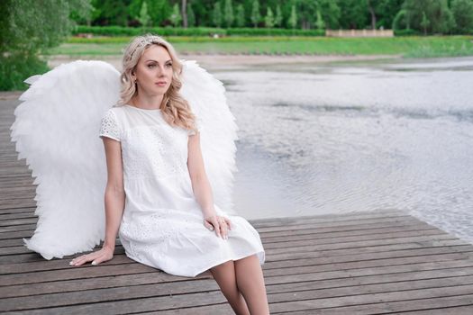 beautiful angel in white dress. Amazing blond woman with long curly hair and white wings