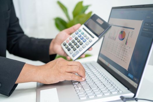 Asian accountant working and analyzing financial reports project accounting with chart graph and calculator in modern office, finance and business concept.