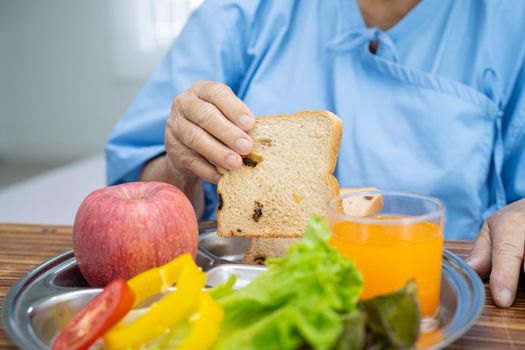 Asian senior or elderly old lady woman patient eating breakfast vegetable healthy food with hope and happy while sitting and hungry on bed in hospital.