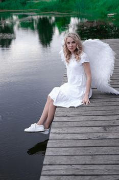 charming blonde with white angel wings standing by the water. beautiful woman in angel costume. goddess.