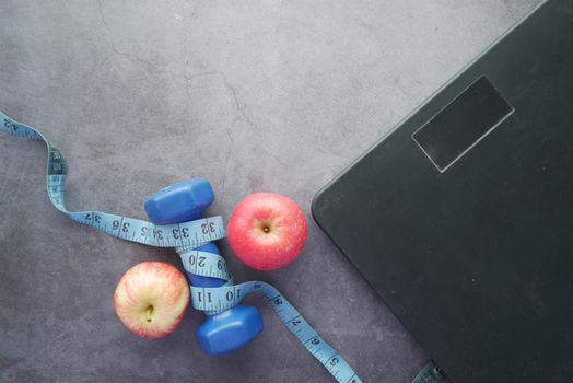 Fitness concept with dumbbell, apple and weight scale on black ,