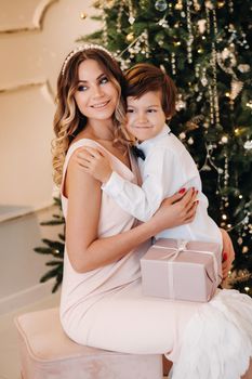 Mom gives her son a Christmas present near the Christmas tree.Happy family.