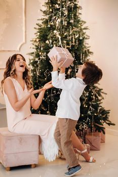 Mom gives her son a Christmas present near the Christmas tree.Happy family.