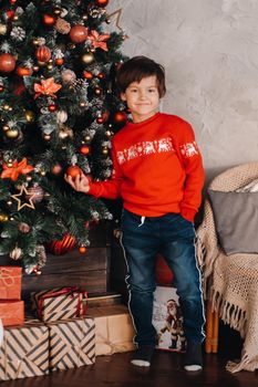 portrait of a smiling boy standing at the Christmas tree at home.