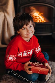 portrait of a smiling boy with a gift in his hands near the fireplace at home.