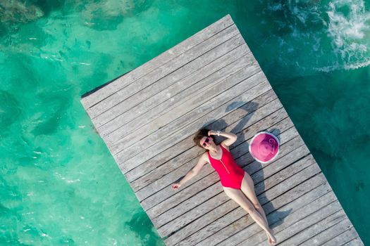 Top view of woman lying down on wooden pier at sunny summer day in Cancun, Mexico. Young sexy woman in the red swimwear in Caribbean. Summer beach vacation concept