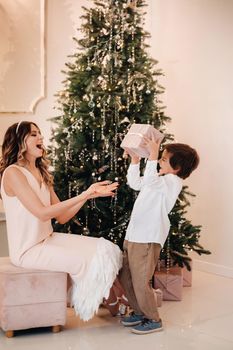 Mom gives her son a Christmas present near the Christmas tree.Happy family.