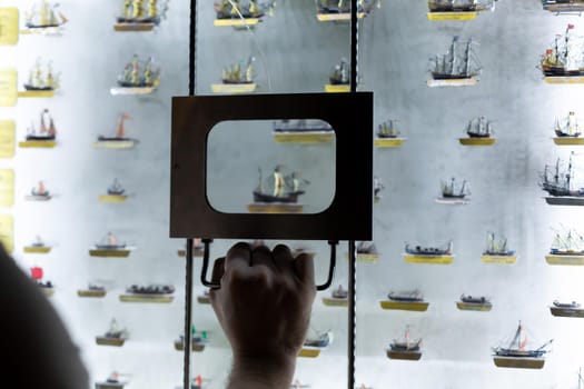 Person examines models of ships through a magnifying glass. An exhibit in the museum.