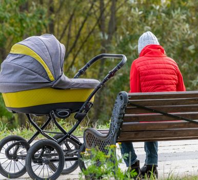 A young mother sits on a park bench, next to a stroller with a child, Moscow Russia