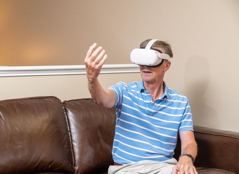 Senior man reaching for object on a modern virtual reality VR headset in home
