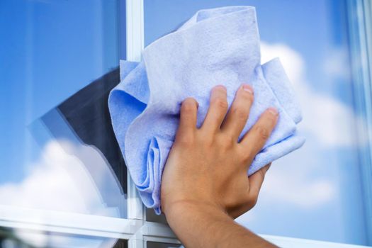 A woman's hand holds a cloth to wipe surfaces and washes the windows of her house to perfect cleanliness and freshness, a creative concept with a close-up of a reflecting sky.