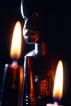 dark close-up of an african statue with two burning candels, one black and the other white