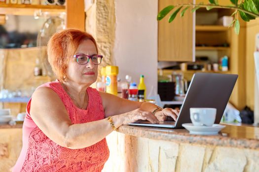 Serious confident elderly woman looking into laptop screen. Female of retirement age in cafe with laptop. Active lifestyle of retirees, technology, family business, 70s people concept