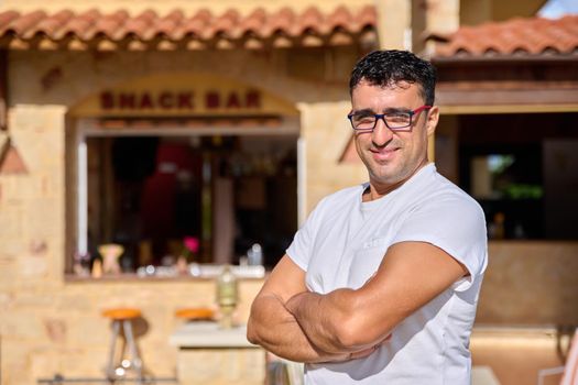 Portrait of positive confident middle aged man wearing glasses with crossed arms. Smiling male cafe bar owner looking at the camera. Small business, 40 people, concept ownership