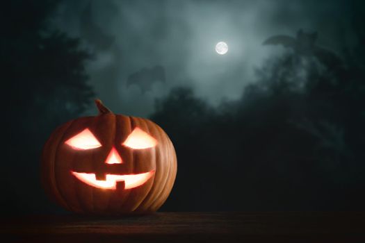 Halloween pumpkin head jack lantern with glowing eyes on a wooden table in the moonlight.