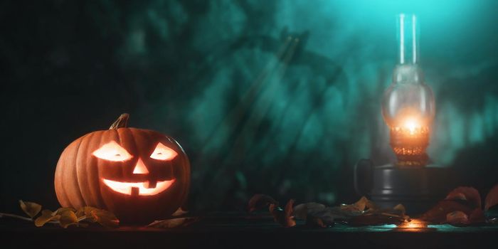Halloween pumpkin head jack lantern with glowing eyes and kerosene lamp on wooden table.
