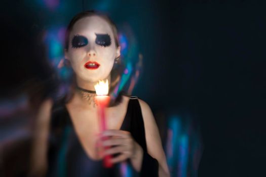 Blurred silhouette of girl with Halloween makeup. She holds candle in hand. Halloween concept on black background. Copy space.