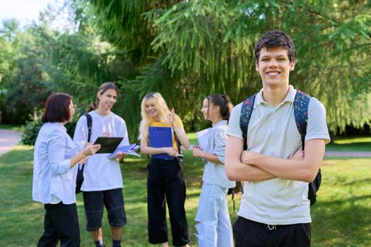 Portrait of male student in park campus, group of teenagers with teacher background. Adolescence, college, high school, education concept.