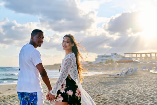 Portrait of beautiful young multiethnic couple holding hands on seashore. Happy romantic loving african man and asian woman looking in camera. People, love, relationship,multicultural family concept