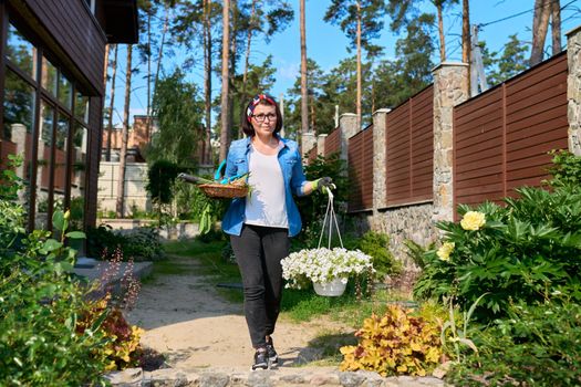 Middle-aged woman in backyard with gardening tools and blooming petunia in pot. Plant and flower care in garden, hobbies and leisure, spring season, gardening, lifestyle concept