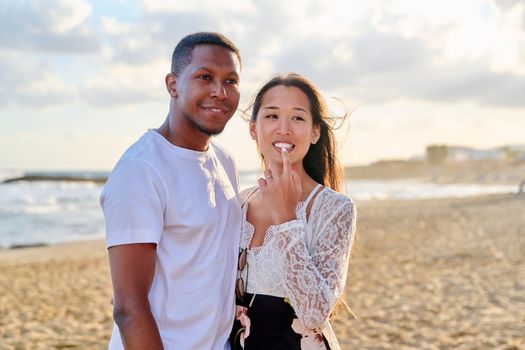 Loving romantic hugging young multiethnic couple on seashore. Happy african man and asian woman together. Love, relationship, dating, happiness, multicultural family, tourism, travel, people concept
