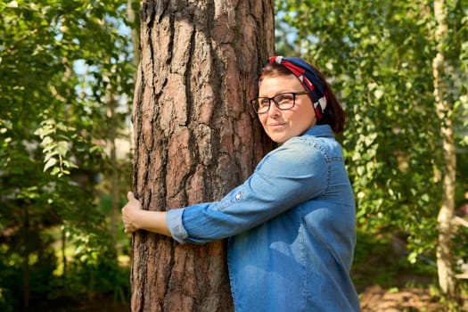 Middle aged woman hugging a tree, energy of nature. Relaxation, mental health, rest, freedom, mature people concept