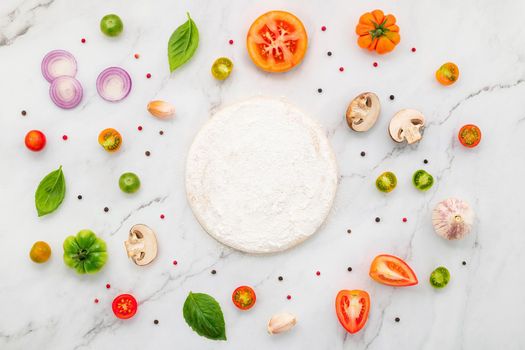The ingredients for homemade pizza set up on white marble background.