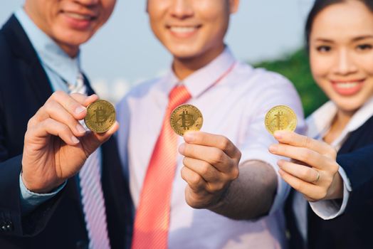 Young Asian Businessman holding golden bitcoin in front of his international Multi ethnic team in modern city.