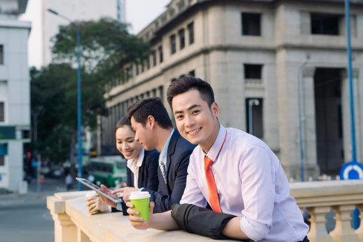 Asian business woman and men having coffee break outside in front of building