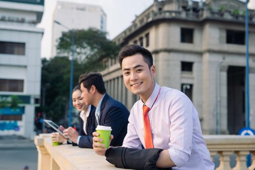 Asian business woman and men having coffee break outside in front of building